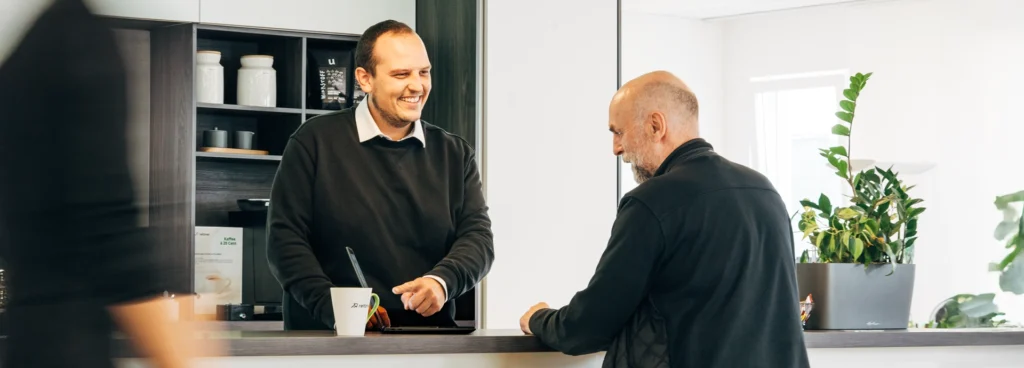 Ein reitzner Berater und ein Kunde stehen sich an einer Theke der Büroküche im Gespräch gegenüber. Thema Network-Security.
