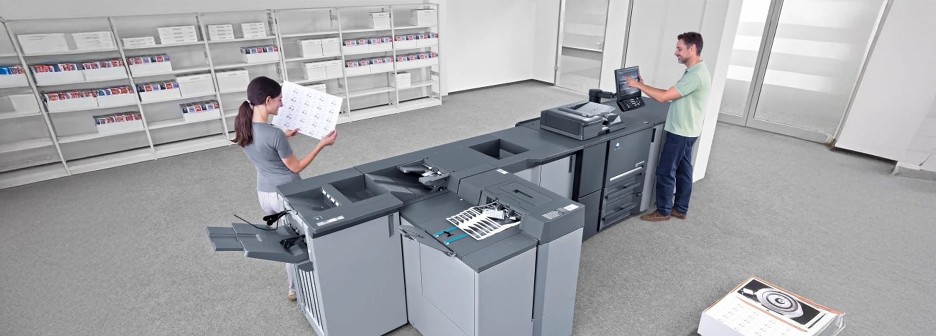 Zwei Personen befüllen eine Digitaldruckmaschine im stehen.